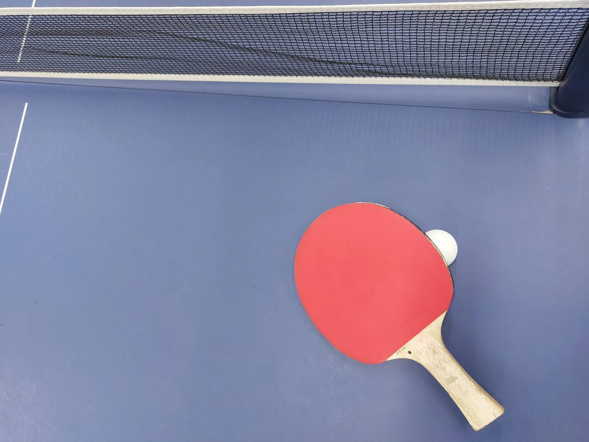 Ett pingisracket och en boll på ett blått bord