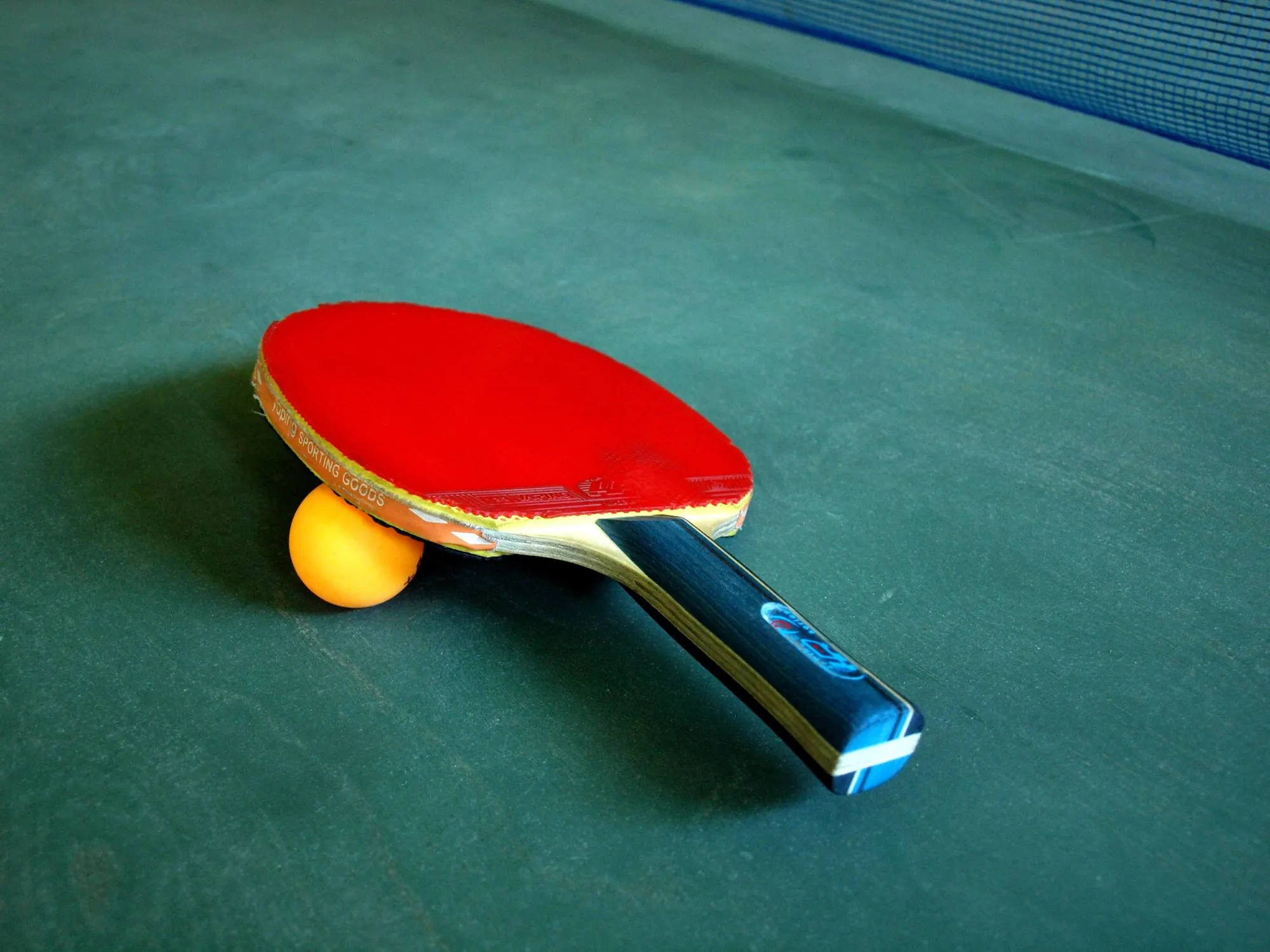 Ett rött pingisracket och en orange boll på ett grönt bord